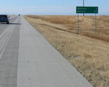 Highway next to an open field with and a green road sign